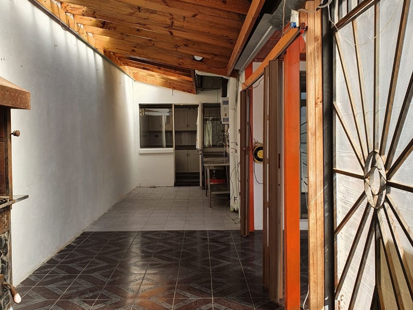 Galería lateral techada con entramado de pérgola de madera, piso cerámico y cierre perimetral.