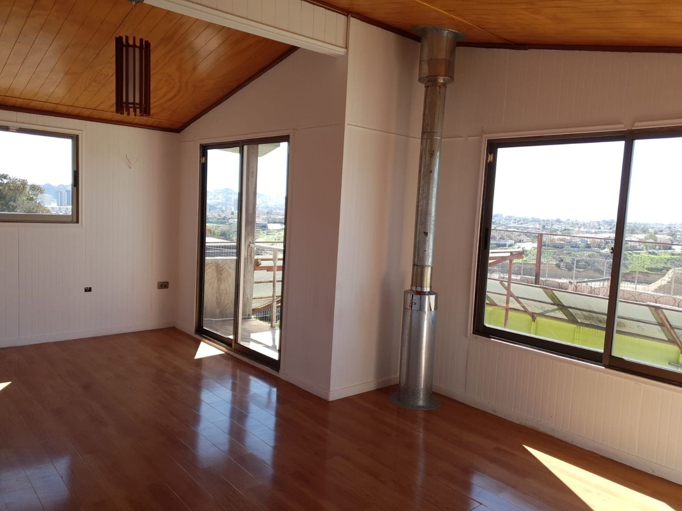 Mansarda en segundo piso con cielo de madera, cañón de estufa y amplios ventanales con vista despejada.