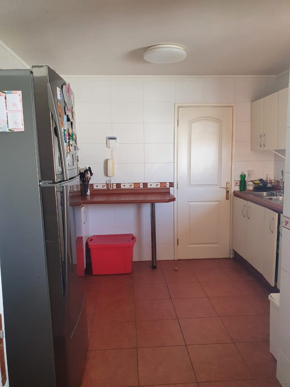Cocina con refrigerador, barra de madera, puerta blanca cerrada y muebles bajo el mesón.
