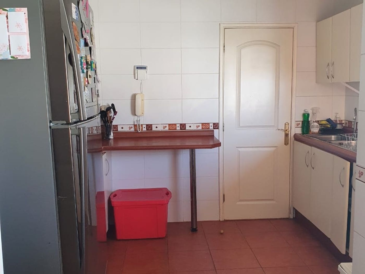 Cocina con refrigerador, barra de madera, puerta blanca cerrada y muebles bajo el mesón.