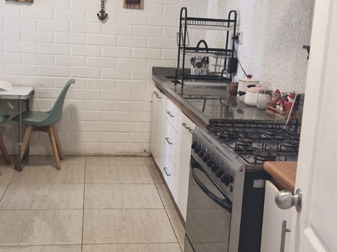 Cocina con pared de ladrillo pintado blanco, cocina a gas, mesa pequeña y reloj decorativo.