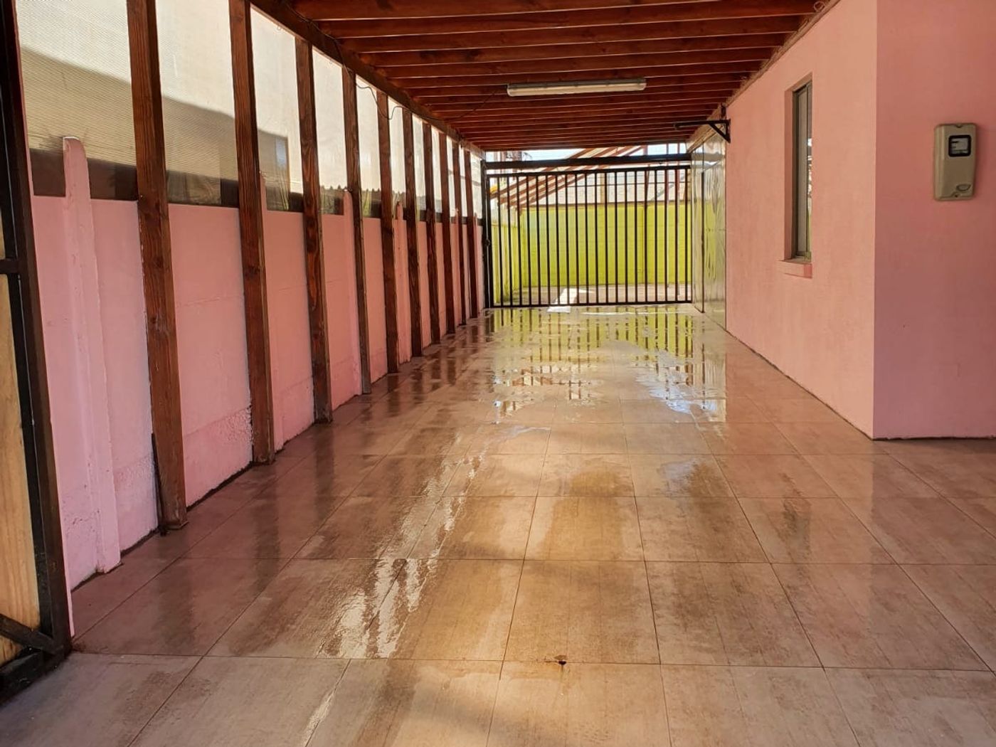 Estacionamiento techado lateral con vigas de madera a la vista y piso cerámico brillante.
