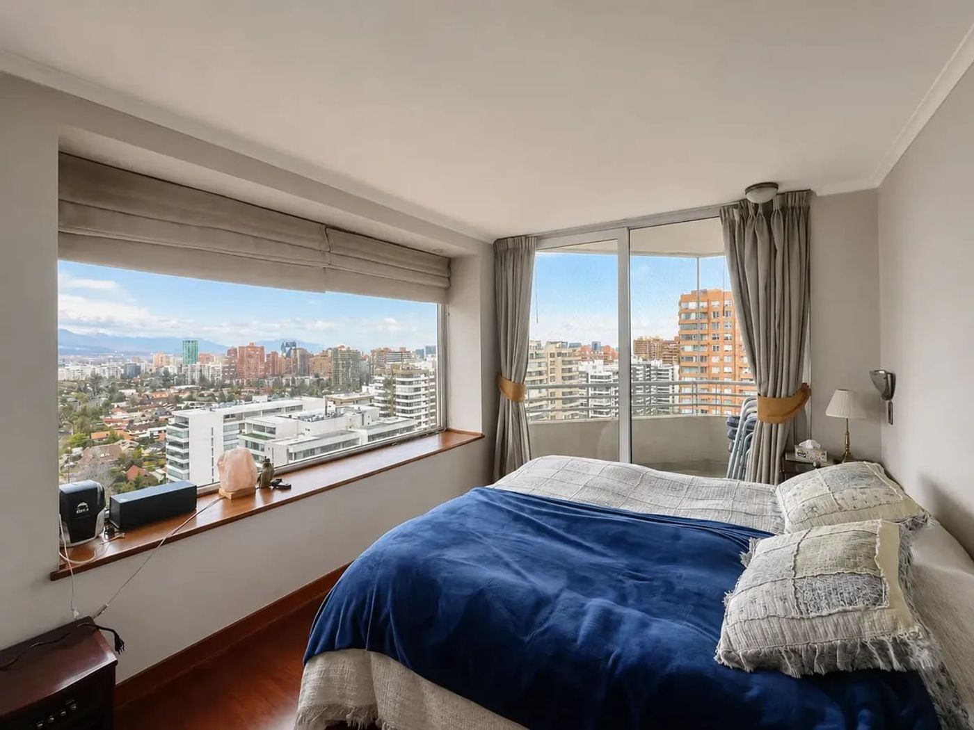 Dormitorio con cama azul, ventanal panorámico y balcón