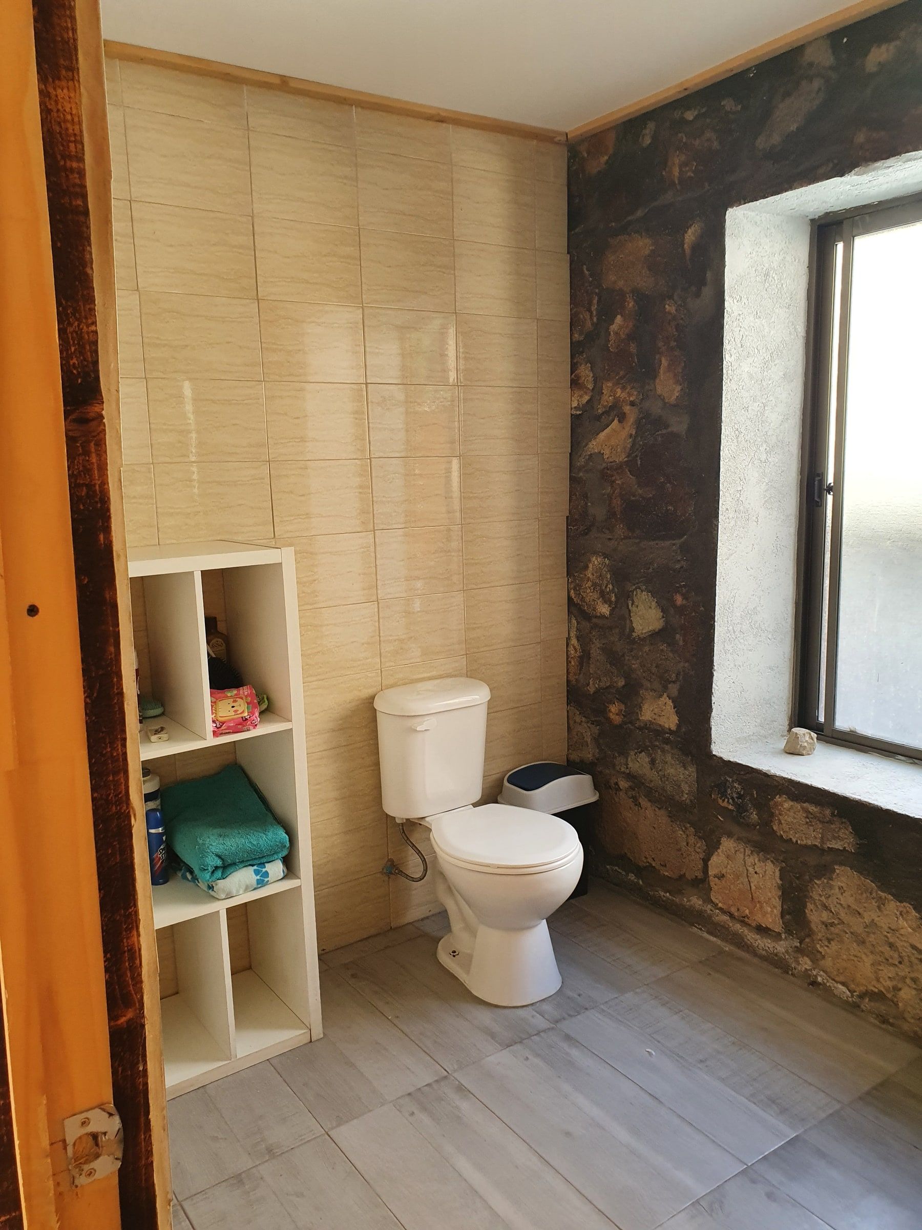 Baño con WC, repisero blanco y ventana de piedra