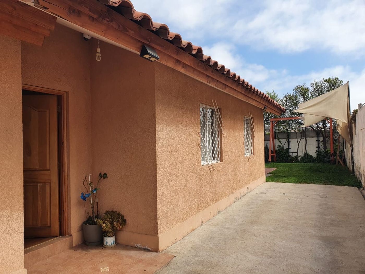 Fachada lateral de la casa con ventanas enrejadas y patio de cemento junto al muro.