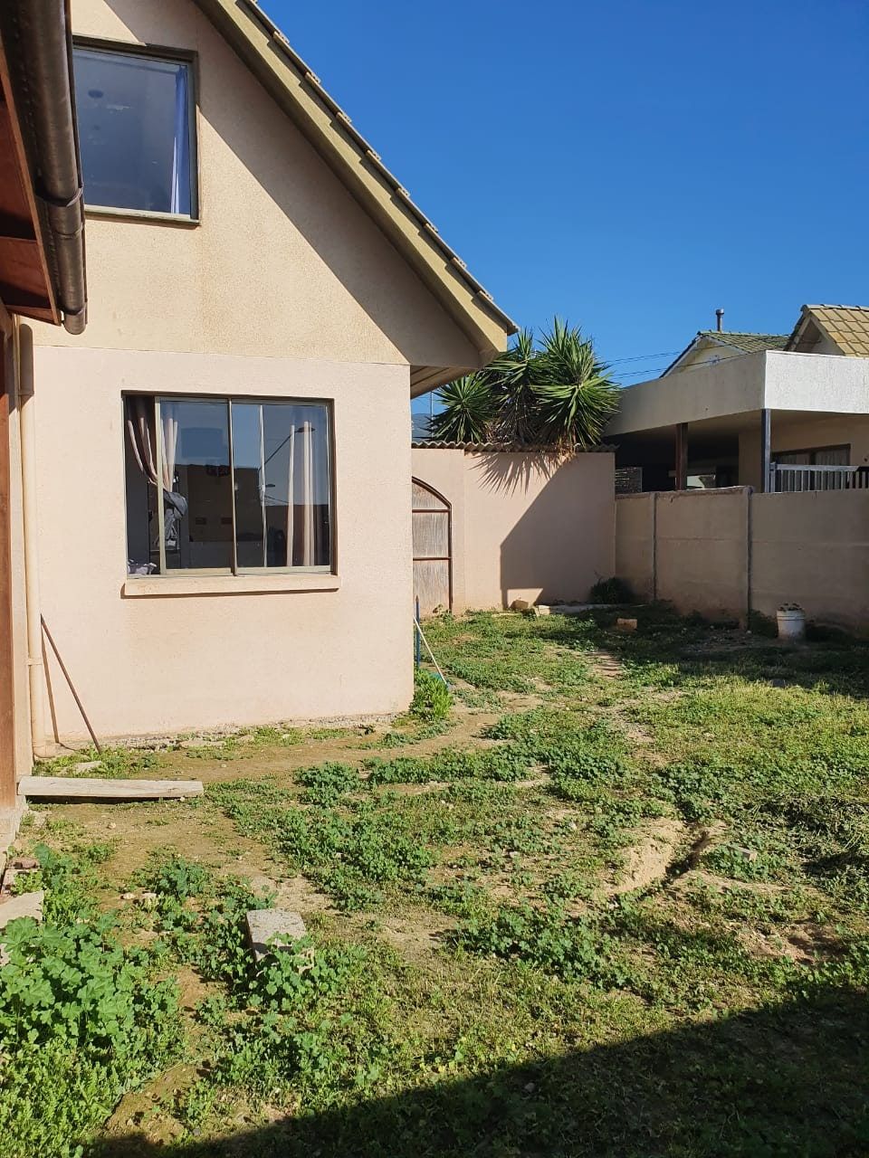 Costado de la casa con ventanas, pasto y muro perimetral hacia el vecino.