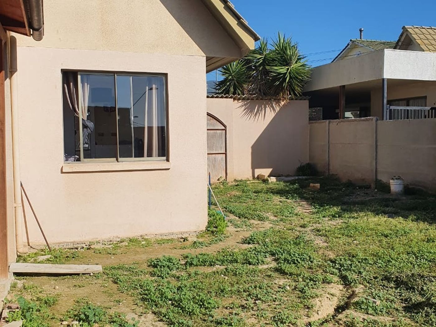 Costado de la casa con ventanas, pasto y muro perimetral hacia el vecino.
