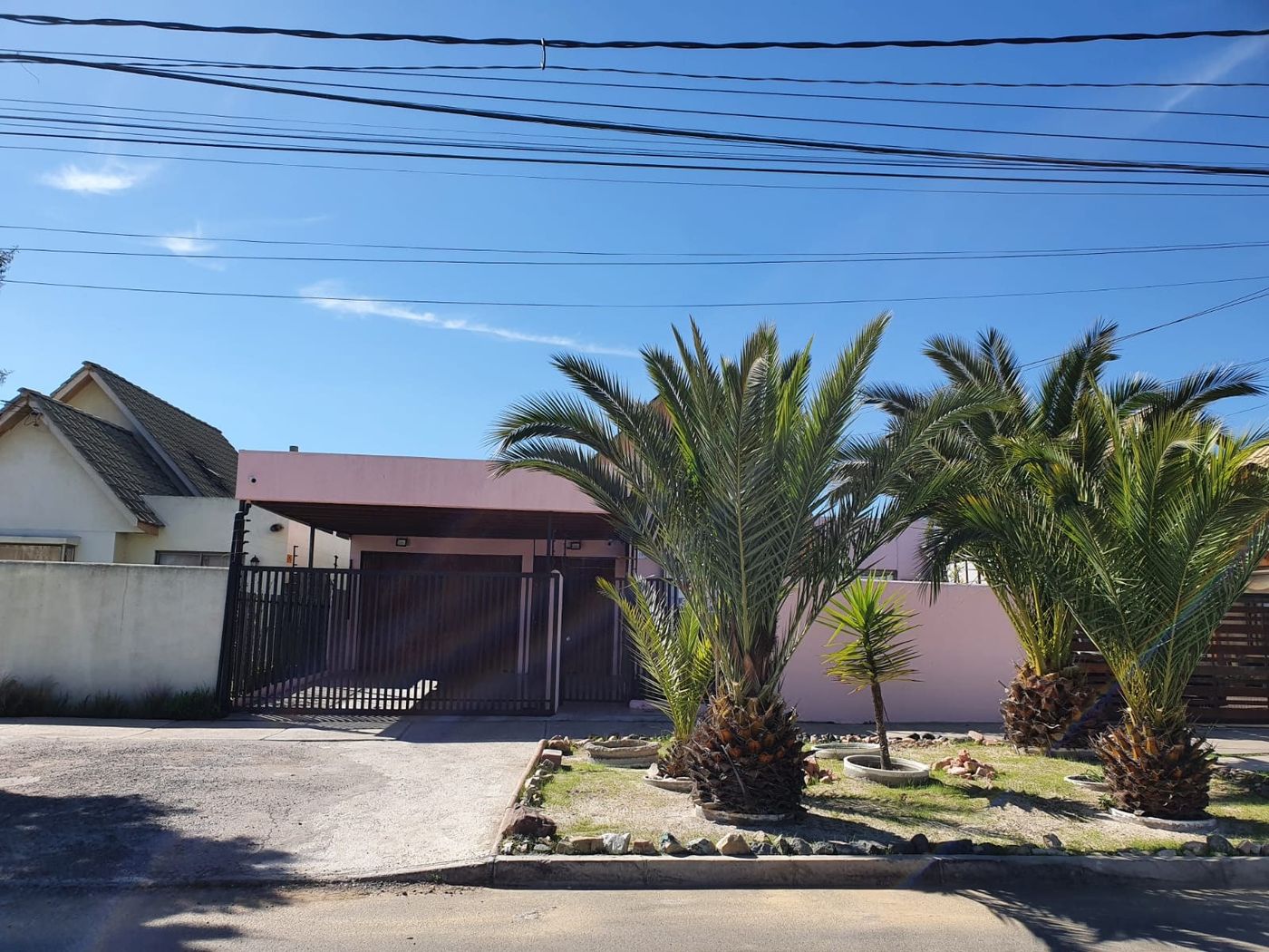 Fachada principal de la casa con dos palmeras en el frontis, cobertizo techado y cielo despejado.