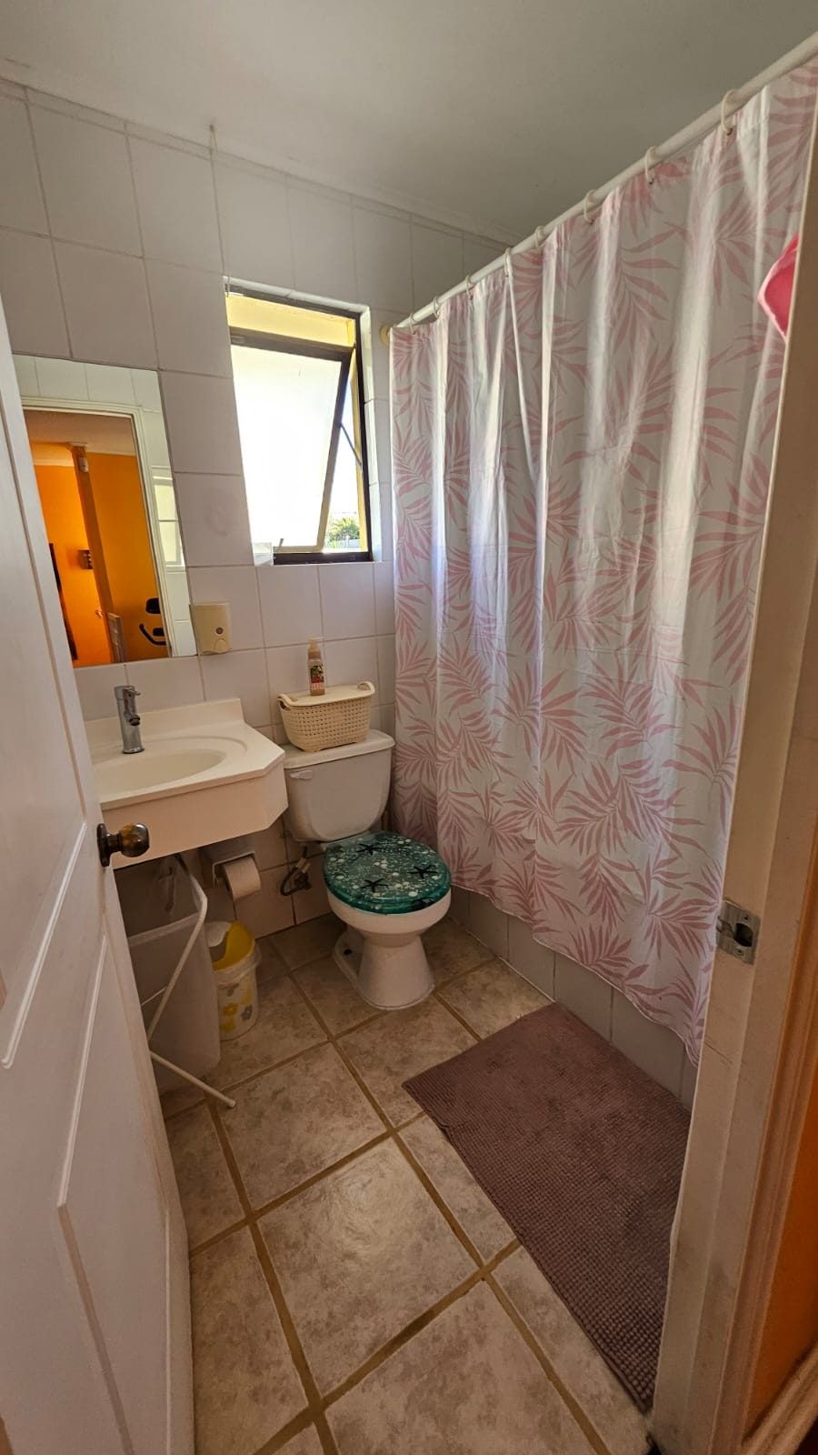 Baño con lavamanos, inodoro, cortina de ducha floreada y ventana con luz natural.