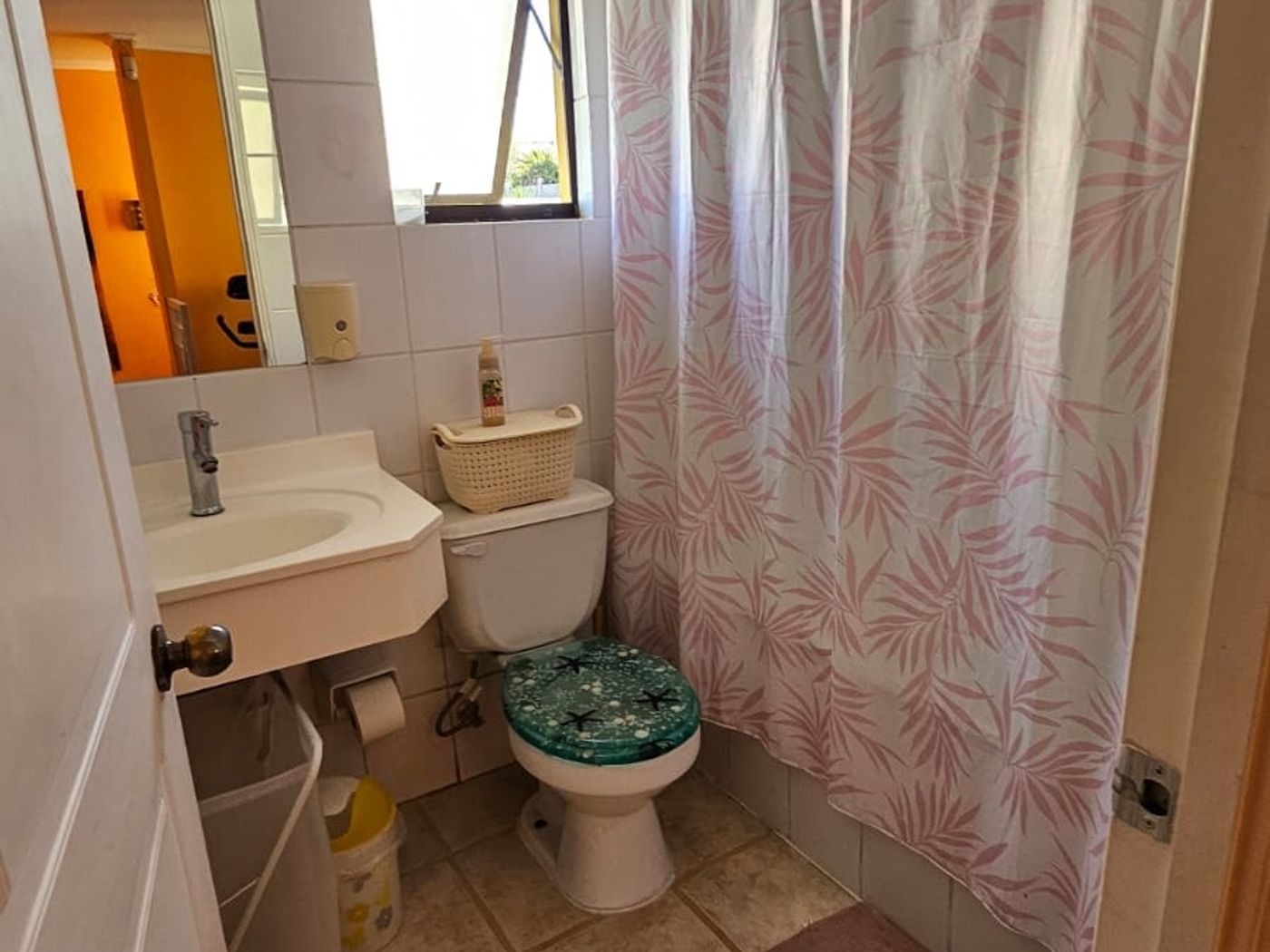 Baño con lavamanos, inodoro, cortina de ducha floreada y ventana con luz natural.