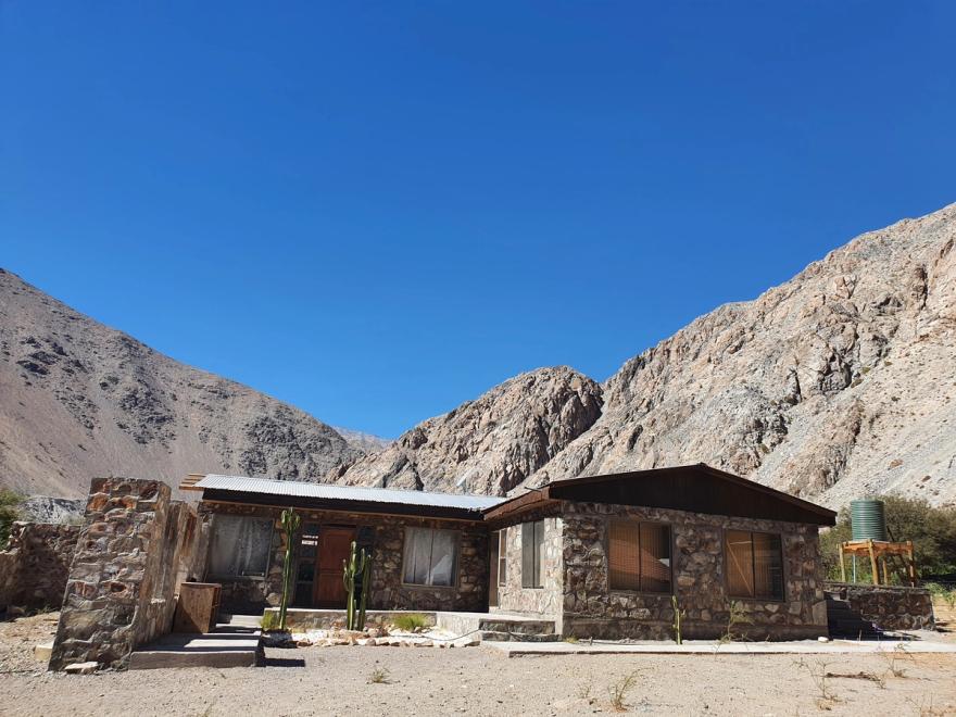 Casa de piedra completa bajo cielo azul y cerros áridos