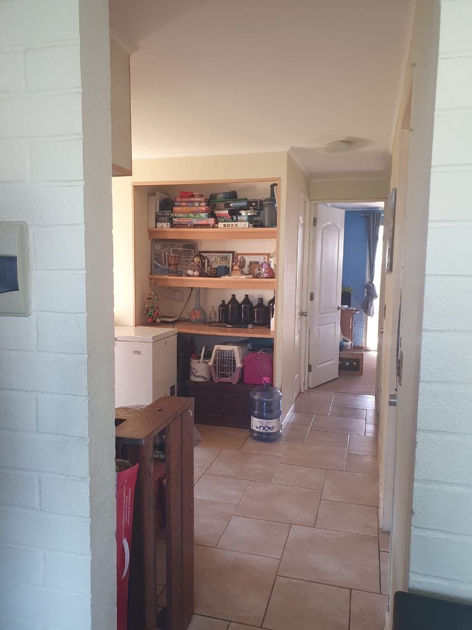 Pasillo interior con repisas de libros, transportadora para mascota y bidones de agua vacíos.