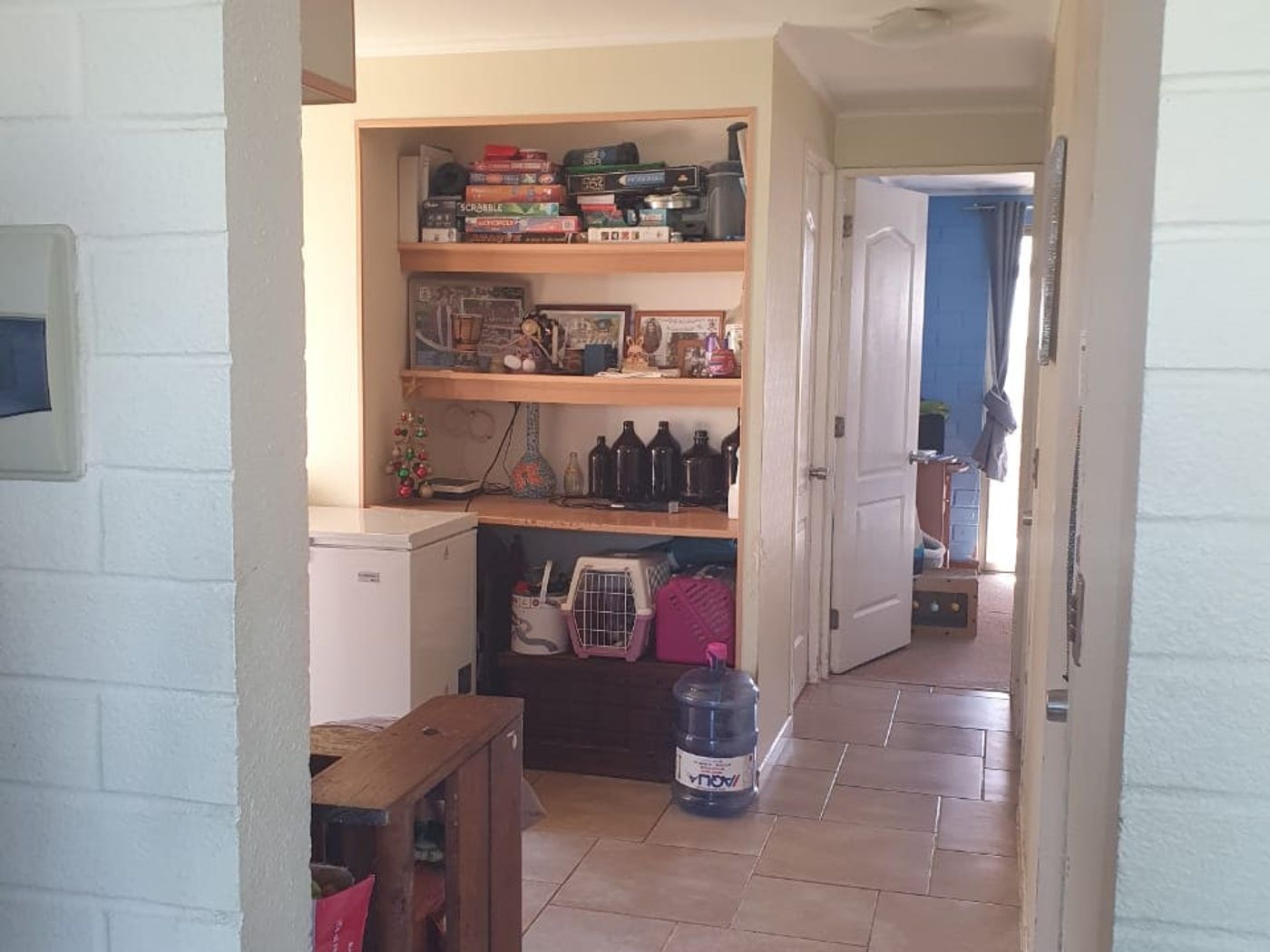 Pasillo interior con repisas de libros, transportadora para mascota y bidones de agua vacíos.