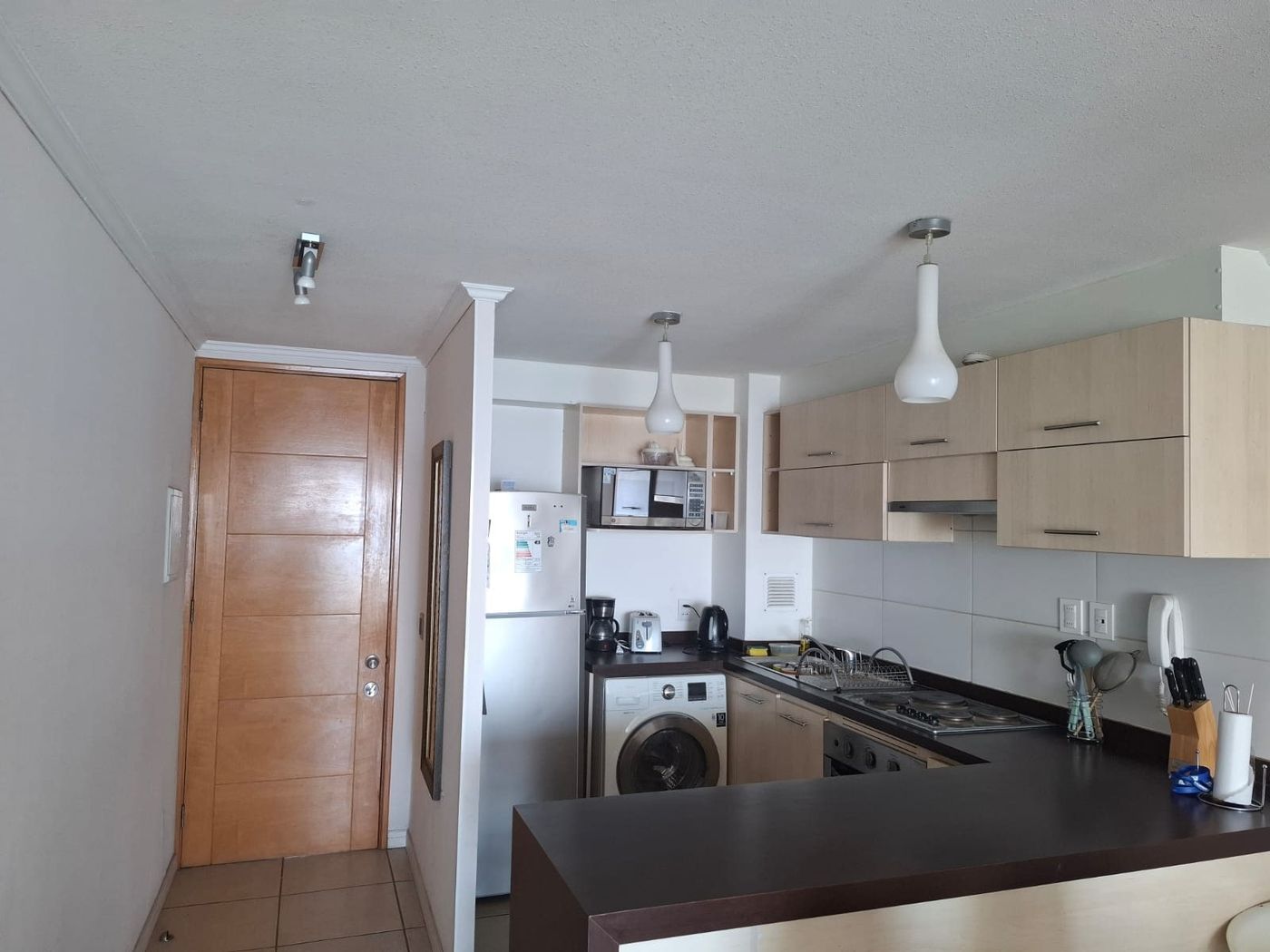 Cocina americana integrada con muebles de almacenamiento, mesón desayunador y refrigerador.