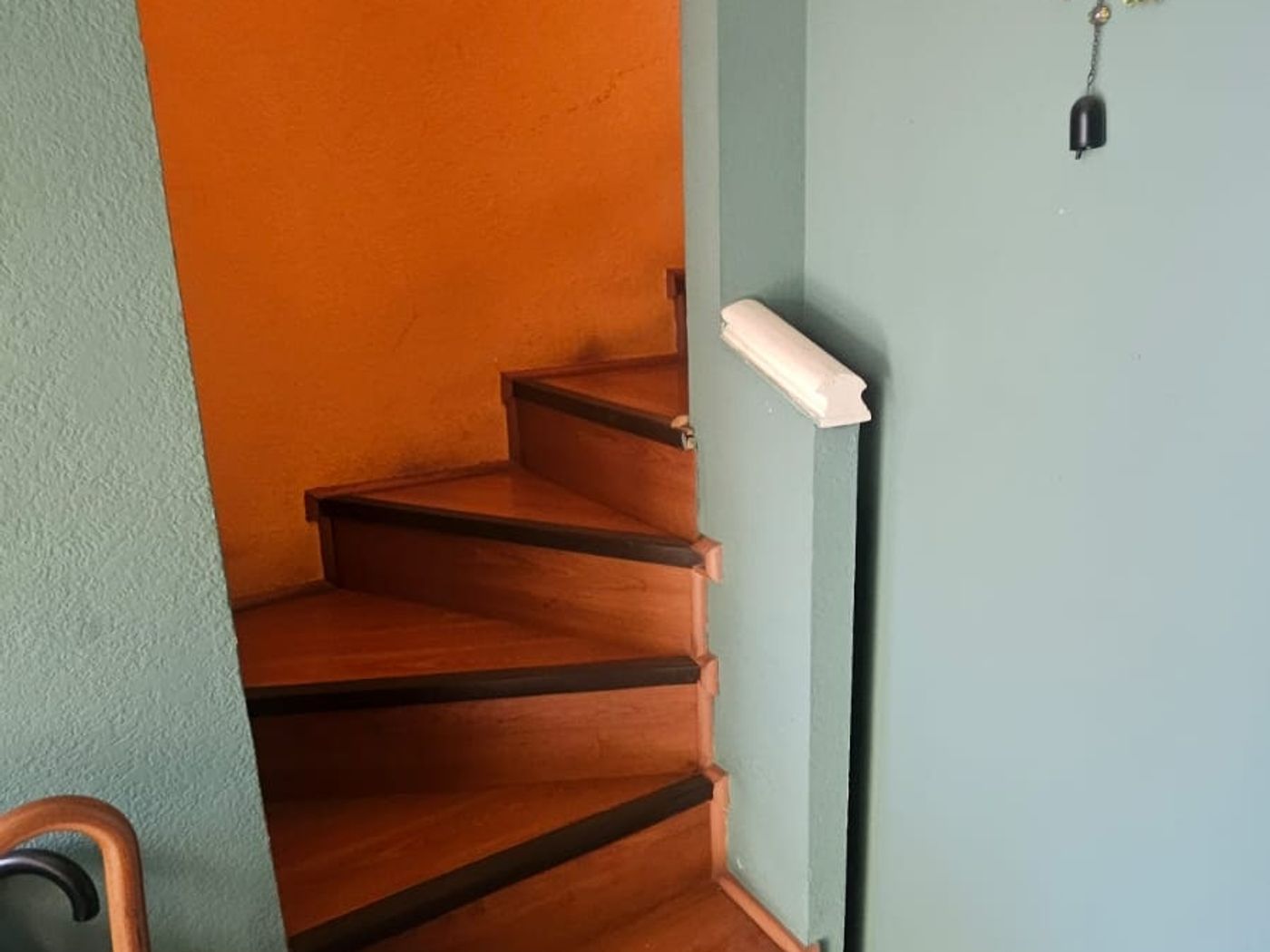 Escalera de madera entre muros naranjo y verde agua, con un adorno de búho colgante en la pared.