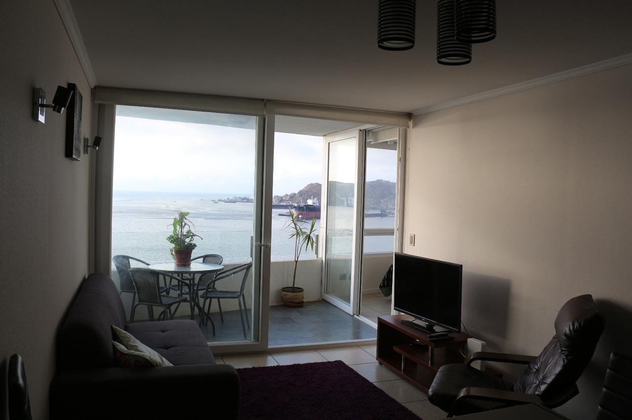 Estar principal con sillón de descanso, mueble para televisión y ventanales con vista a la bahía.