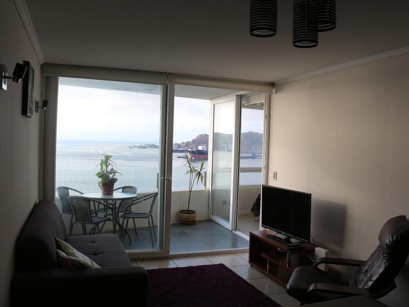 Estar principal con sillón de descanso, mueble para televisión y ventanales con vista a la bahía.
