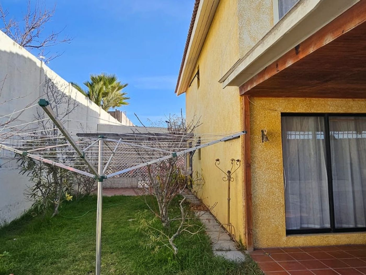 Fachada lateral de la casa amarilla con terraza de baldosas, antena satelital y tendedero de ropa.