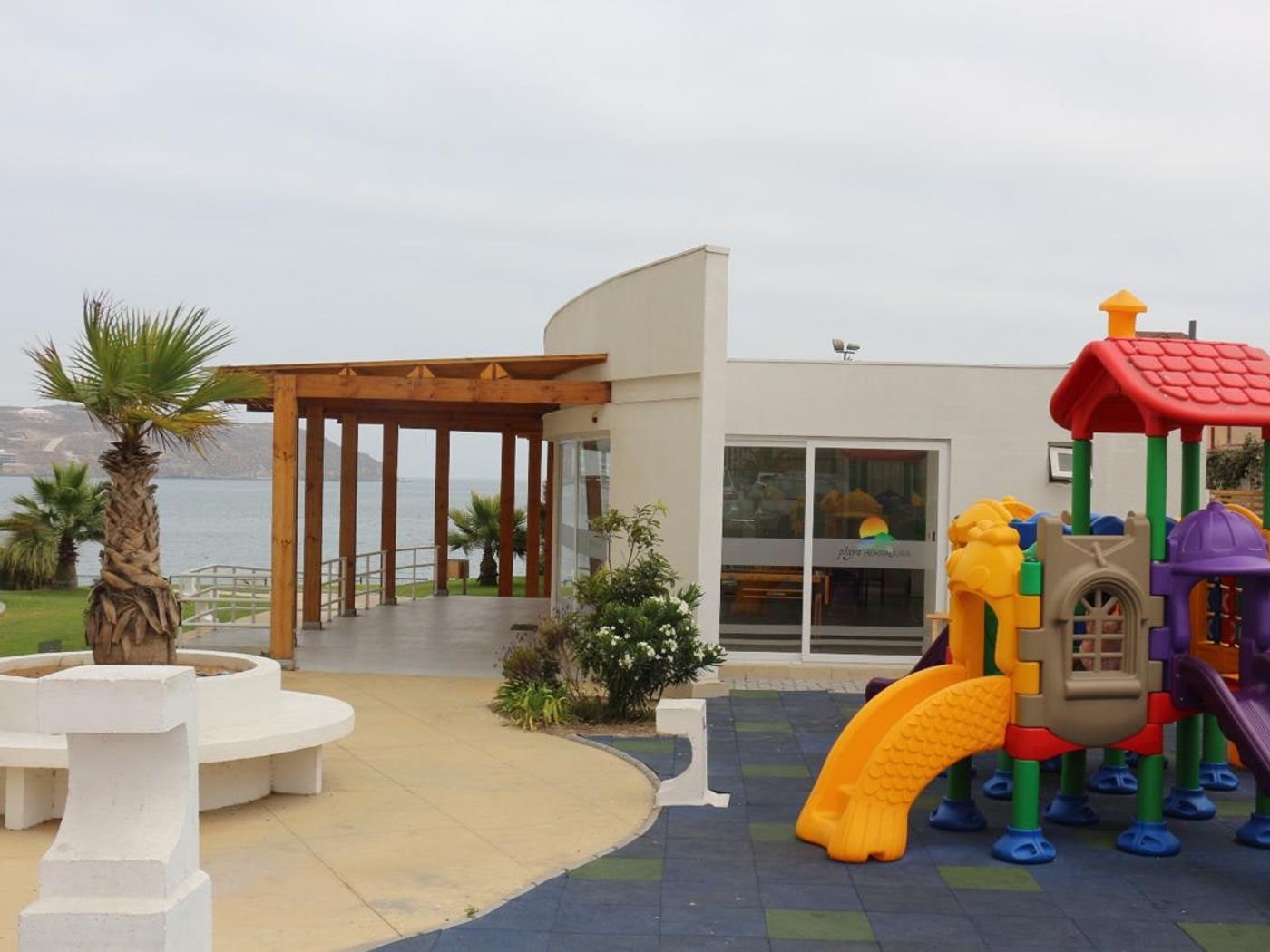 Juegos infantiles modulares en área verde del condominio con vista al mar y la bahía.