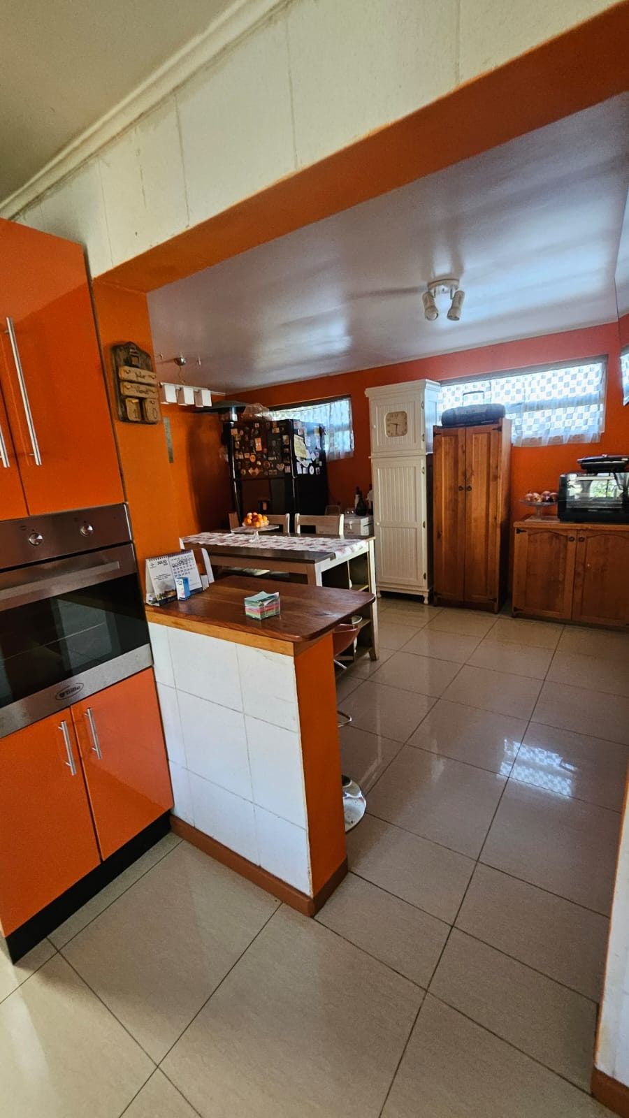 Detalle de cocina con muebles y horno color naranjo, isla central con cubierta de madera.