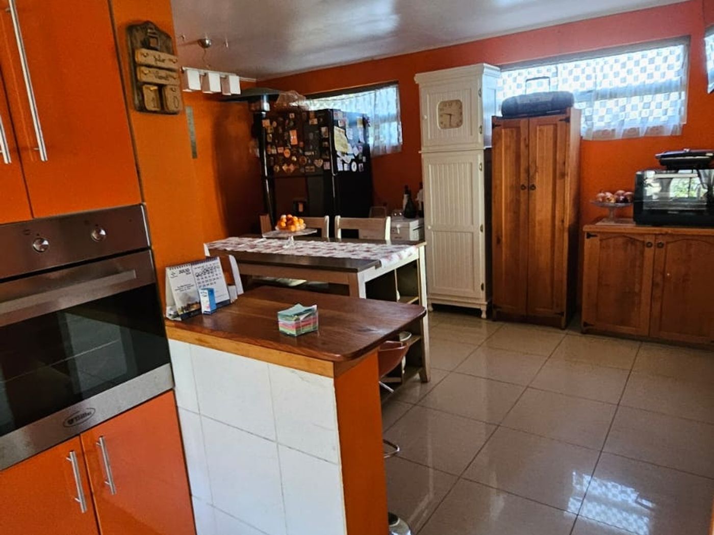 Detalle de cocina con muebles y horno color naranjo, isla central con cubierta de madera.