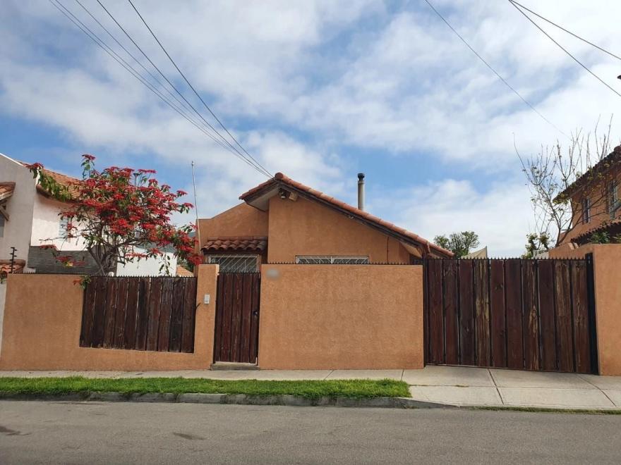 Fachada de la vivienda con antejardín, portón de madera, reja peatonal y techumbre de tejas.