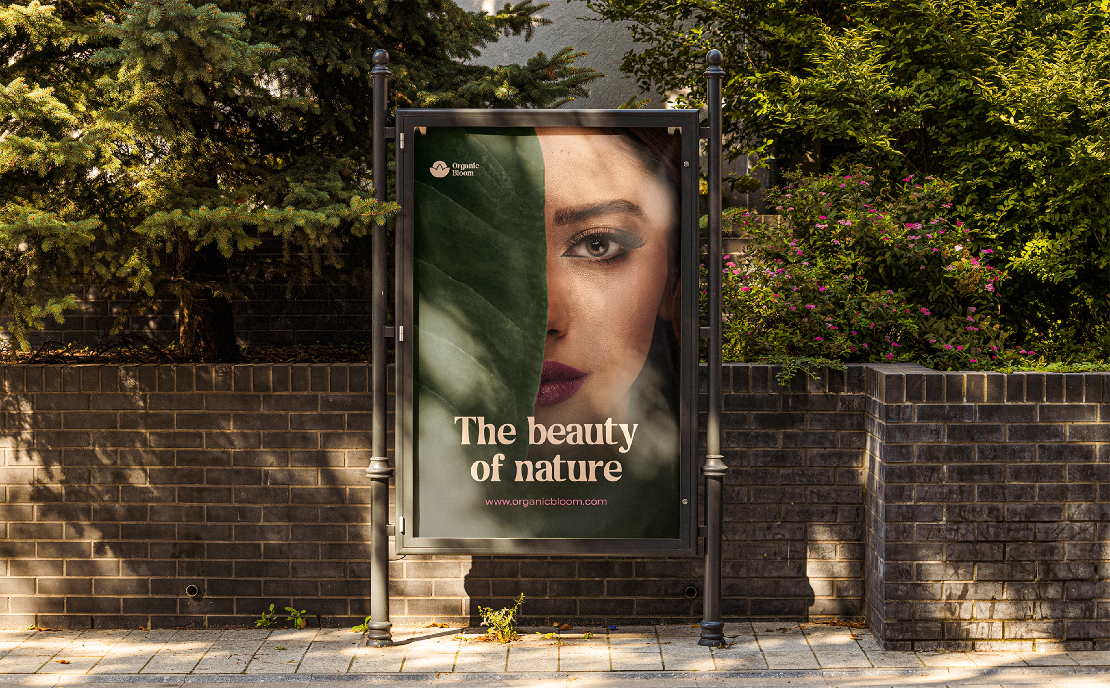 The image shows an Organic Bloom ad on a billboard poster on a street with flowers and trees behind it. The ad contains Organic Bloom's slogan "The beauty of Nature" and the website "www.organicbloom.com" the image shows a woman whos face is half hidden by a leaf