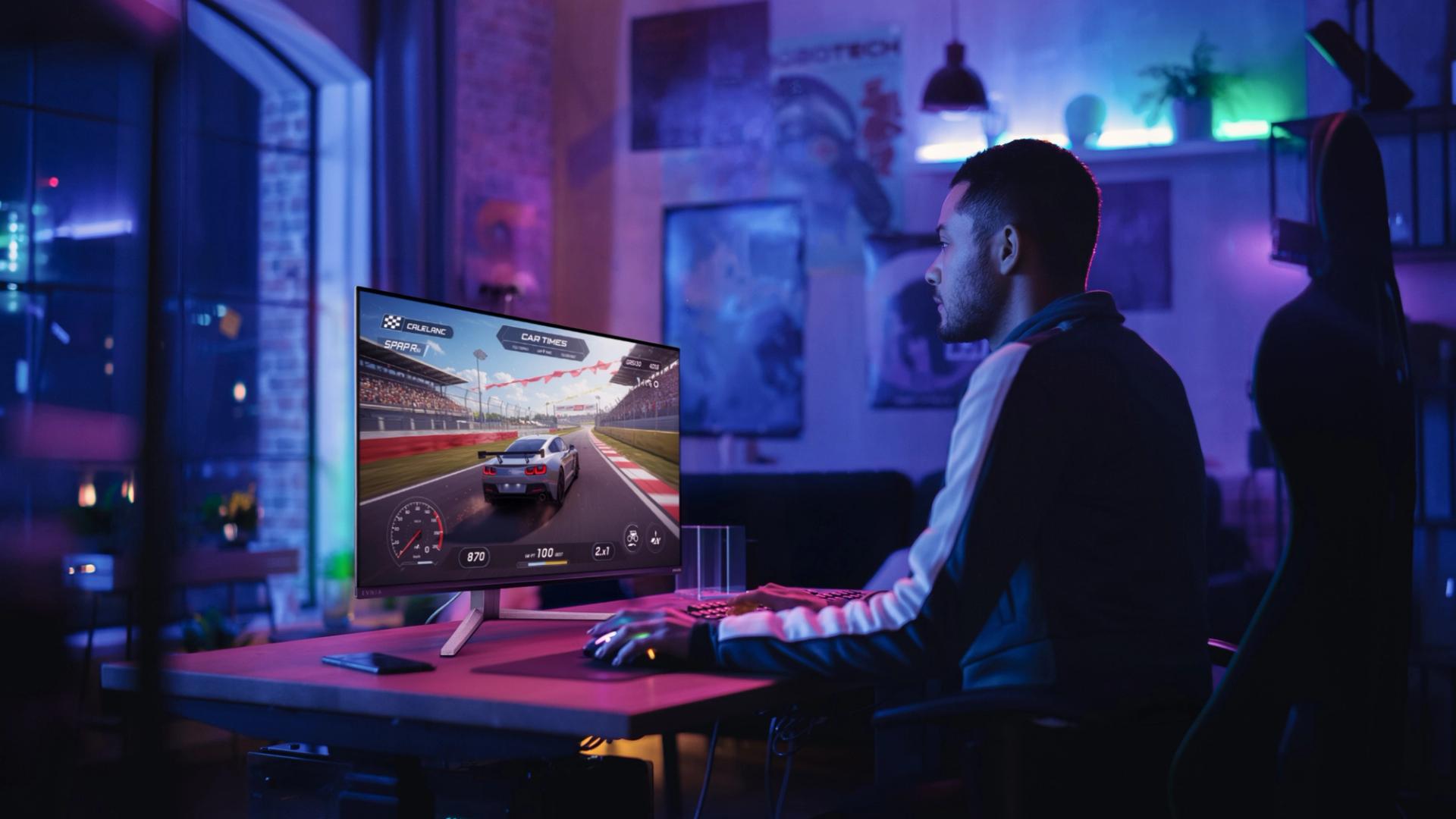 A gamer playing a racing game on a Philips Evnia gaming monitor in a modern gaming room illuminated with colorful ambient lighting.