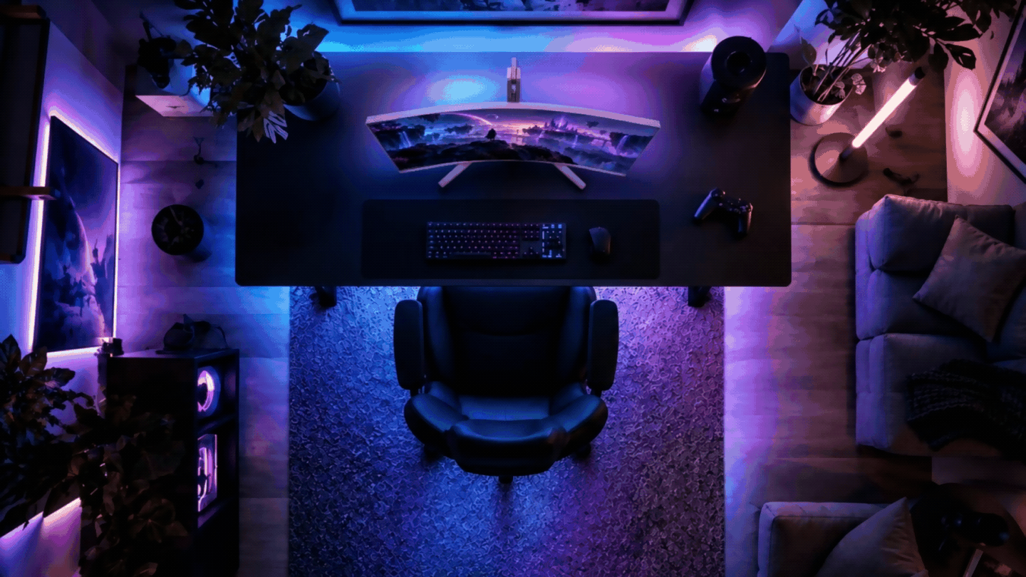 Top-down view of a modern gaming setup featuring a curved ultrawide monitor, black gaming desk, ergonomic chair, and purple-blue RGB lighting in a cozy room.