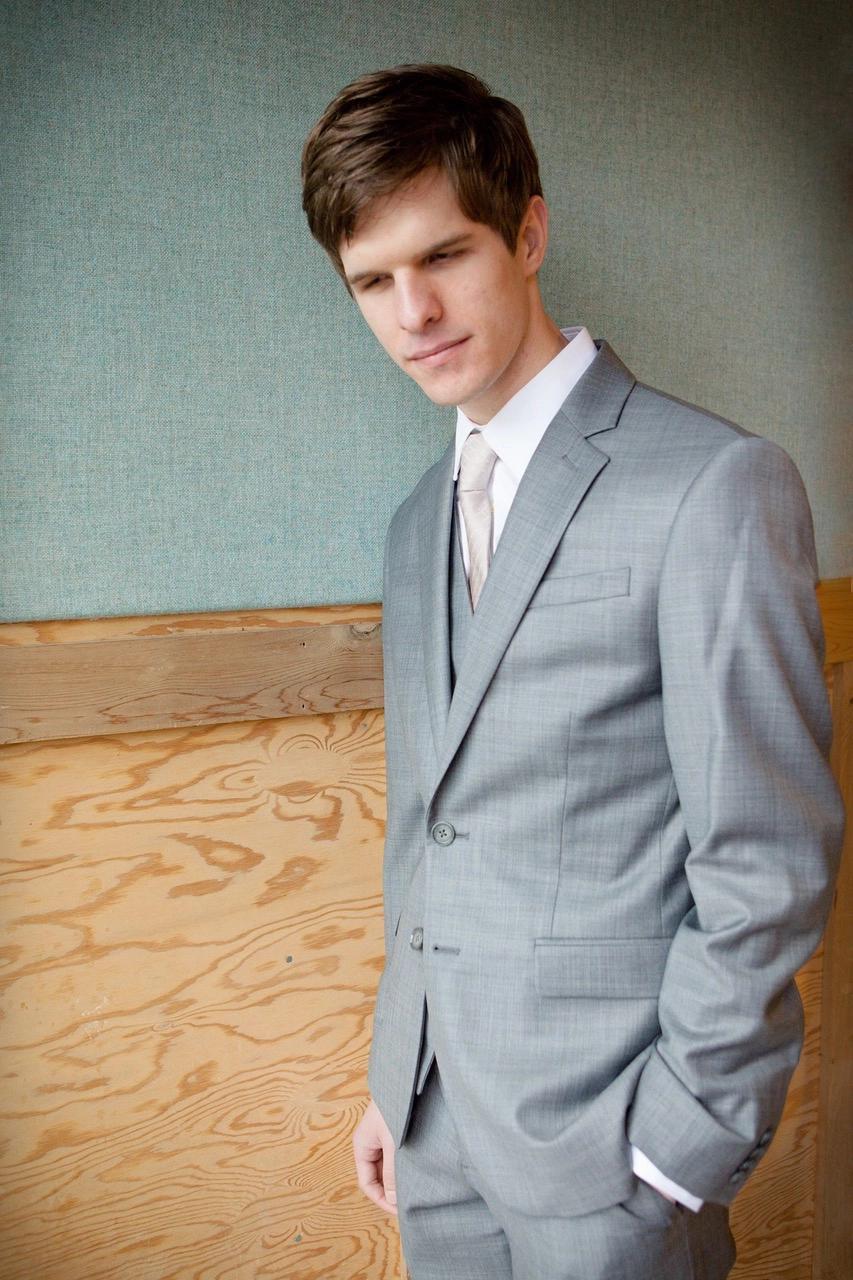 Mac Potts wears a grey suit with a beige tie.