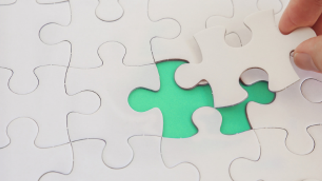 A hand places the final white puzzle piece into the missing spot to complete a blank puzzle. 