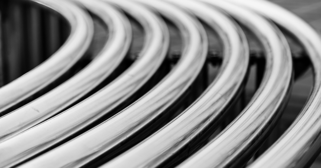 A black-and-white photo of series of silver tubes curving to the left.