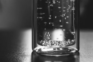 A black and white close up of a glass vial with liquid and bubbles inside.