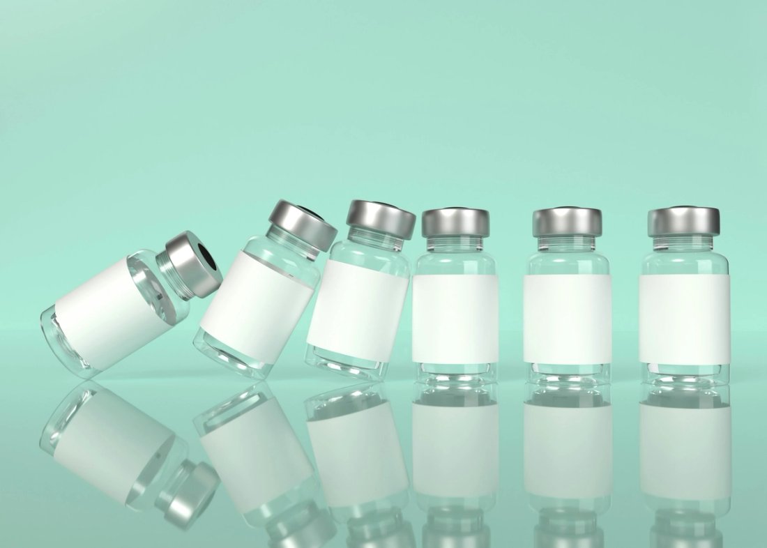 Clear medicine vials falling like dominos against a green background.