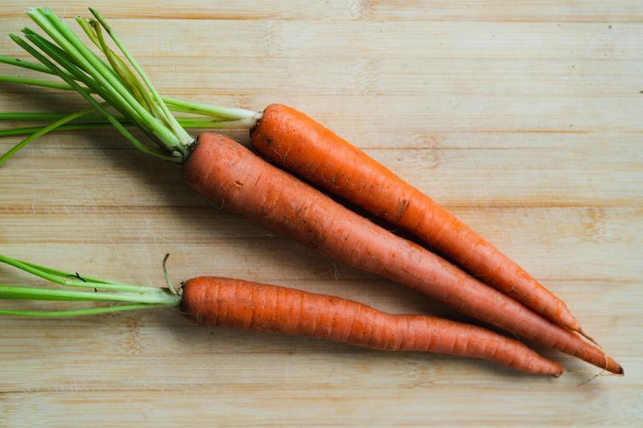 Three raw orange carrots with tops on a cutting board