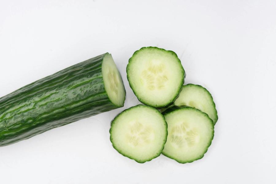 An unpeeled cucumber and round slices on a white surface
