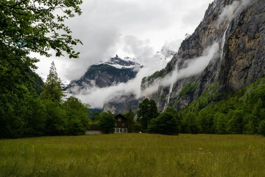 A meadow and wooden house below misty cliffs in Lauterbrunnen