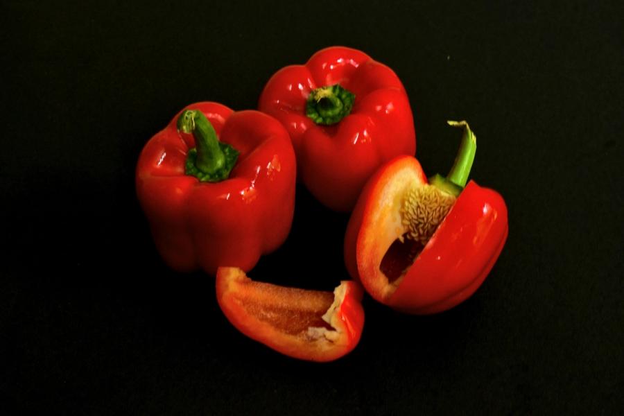Whole and cut red bell peppers on a black surface