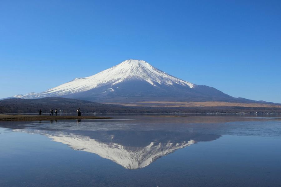 Snow-capped Mount Fuji reflects in still water under a clear blue sky