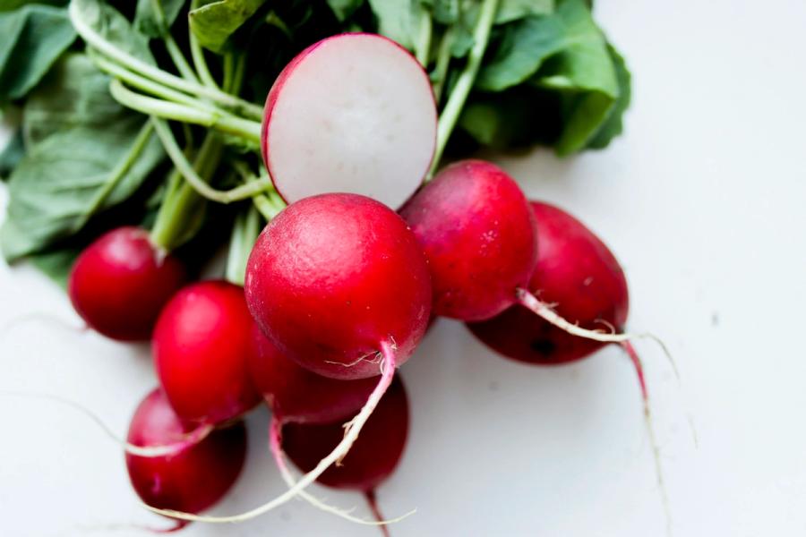 Red radishes with leaves, roots and one sliced open