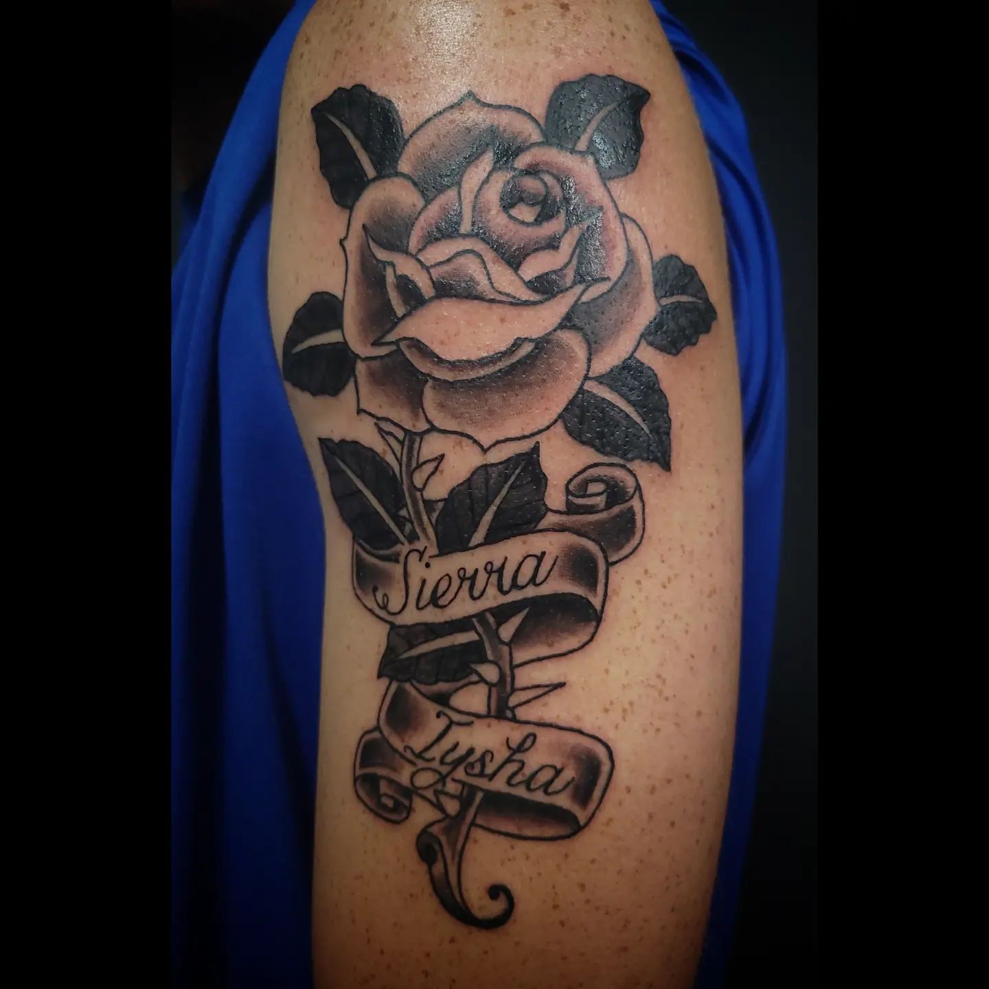 A tattoo of a flower wrapped with the names Sierra and Iysha on a ribbon