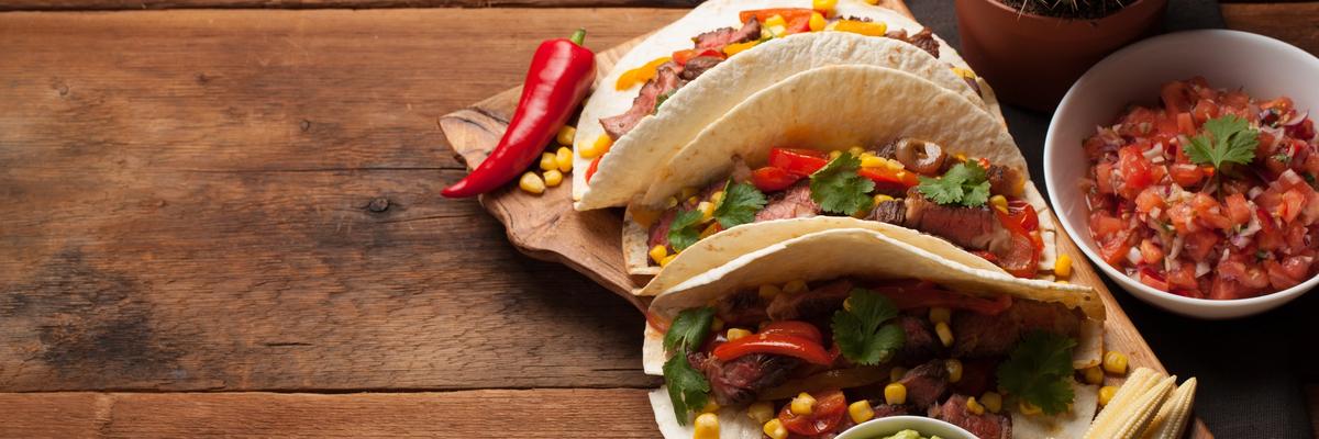 Three Mexican street tacos filled with grilled beef, corn, peppers, and cilantro served with guacamole and fresh salsa.