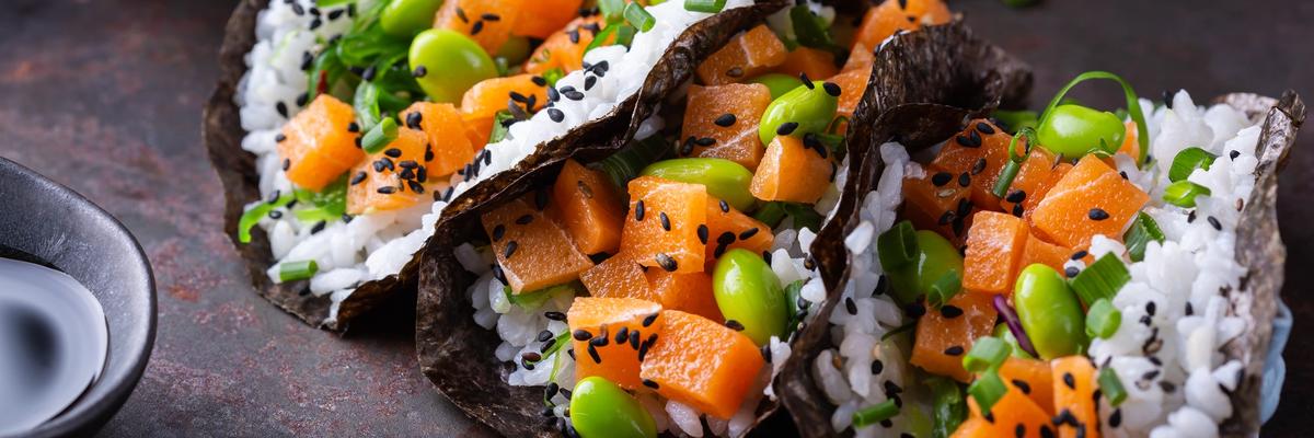 Fusion-style sushi tacos filled with rice, plant-based salmon, edamame, and sesame seeds served on nori shells.
