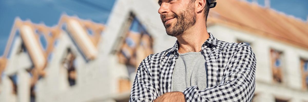 Licensed home builder wearing a hard hat standing confidently in front of a residential home under construction in Utah.