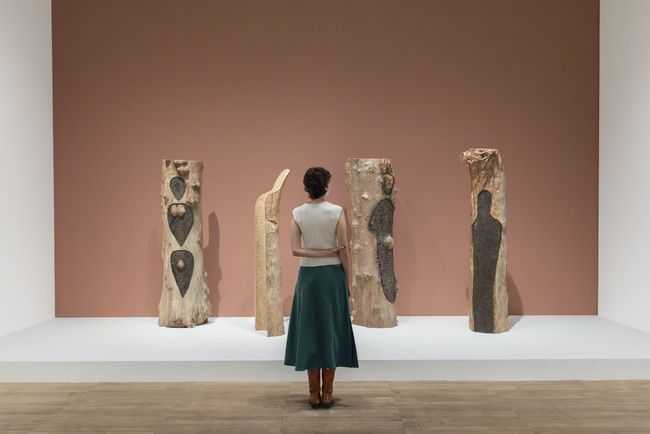 A visitor looks at tree-trunk sculptures marked with human forms