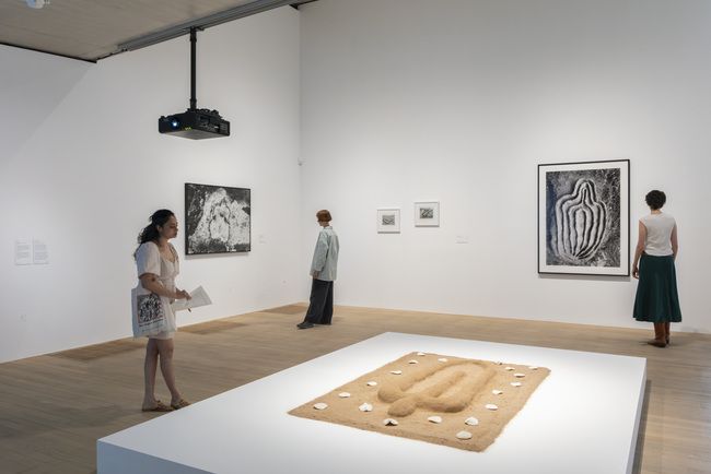 A floor-based sand sculpture is shown with photographs of cave works