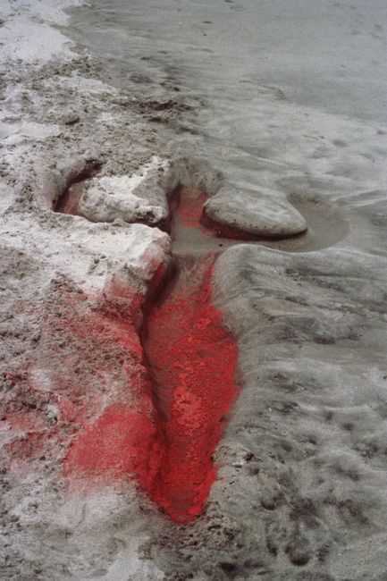 Red colour and sand form a human outline beside the sea