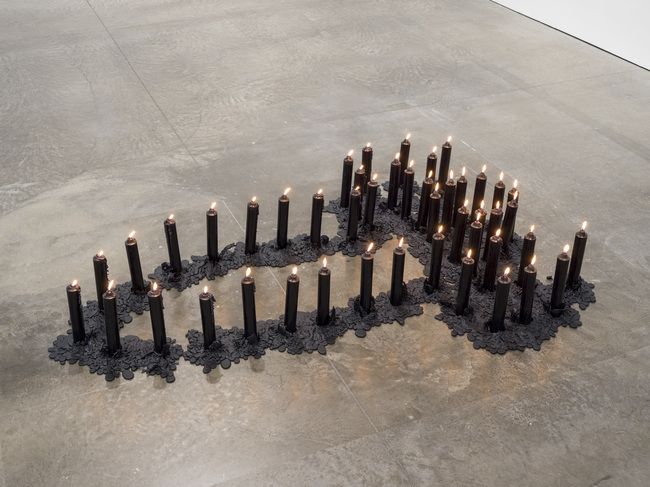 Black candles arranged on the floor form a human outline