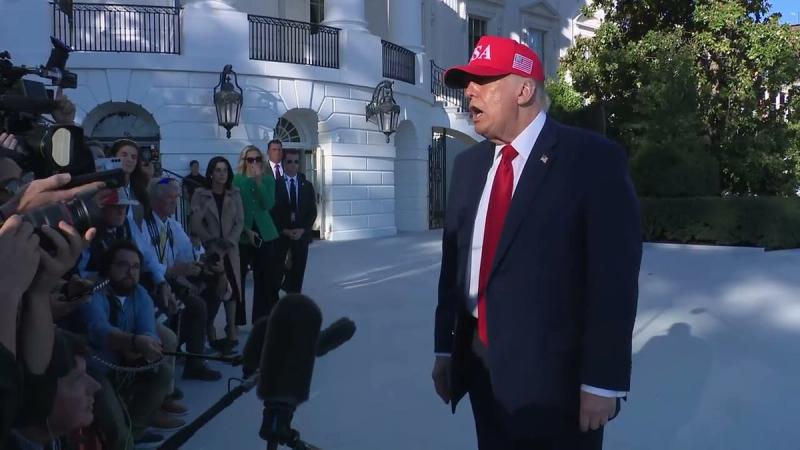 President Trump, in a red USA hat, speaks with reporters on the South Lawn of the White House after returning from Baltimore, October 6, 2026 (still from Official White House video)