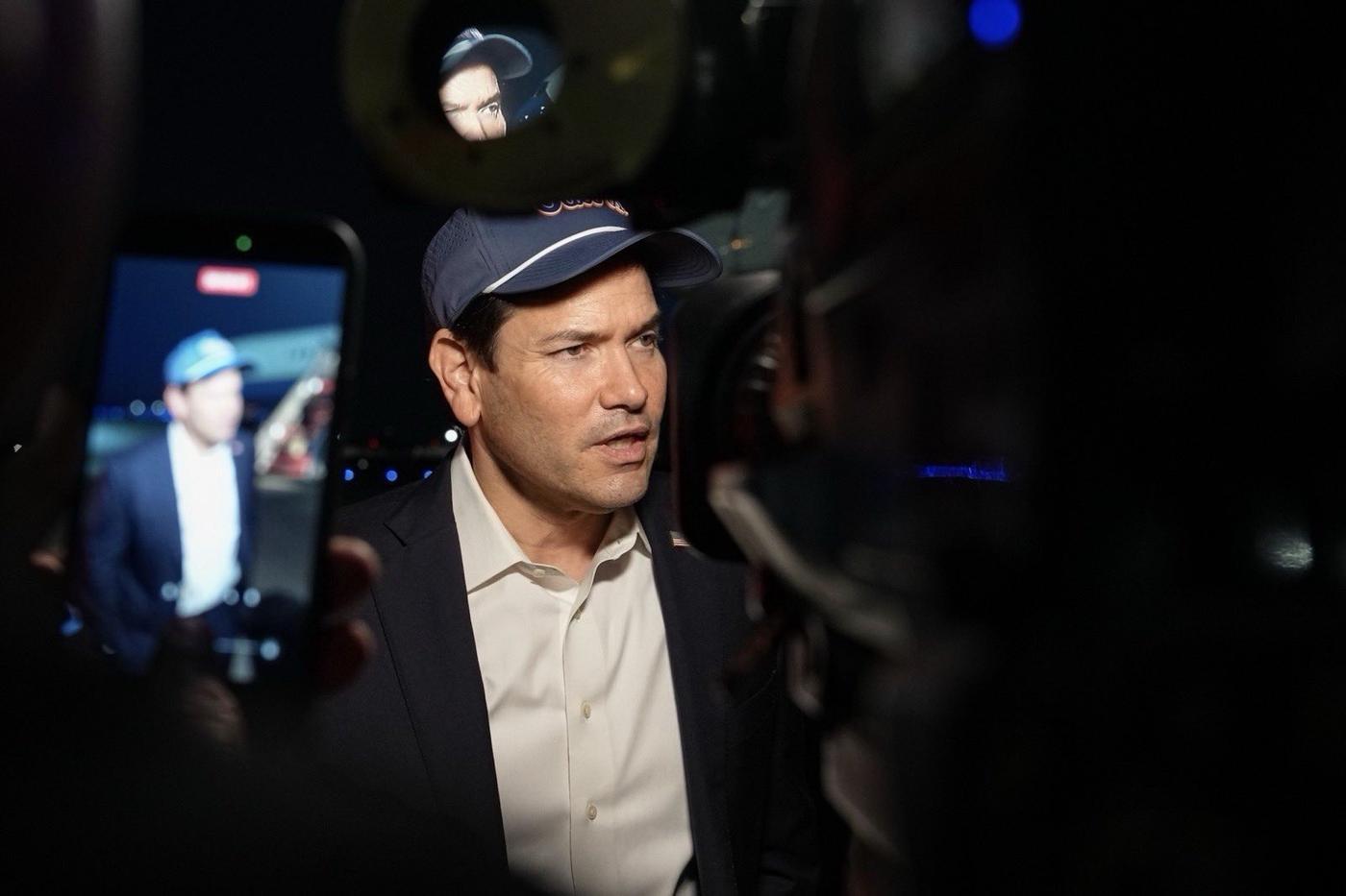 Secretary of State Marco Rubio, wearing a ball cap, speaks with reporters as a phone records him at Joint Base Andrews, Oct. 17, 2026. Secretary Rubio on X, Oct. 17, 2026: “Just departed for Uzbekistan and India to continue securing the Trump Administration's economic opportunities for our nation.”